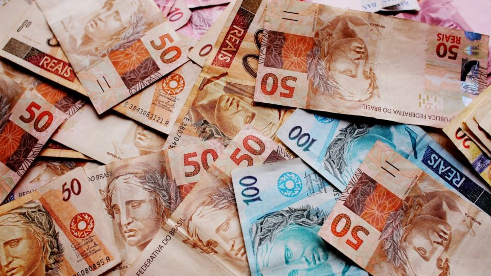 Um monte de notas de dinheiro em espécie espalhados. As notas são grande parte de 100 e 50 reais.