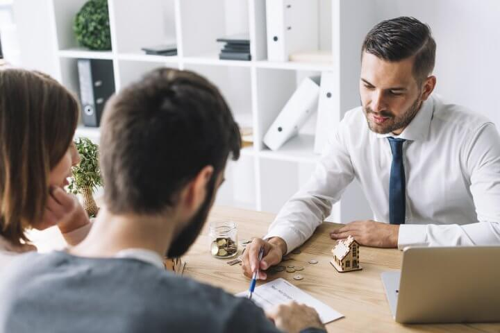 Um homem com terno falando com um casal e negociando um serviço financeiro relacionado a compra de um imóvel