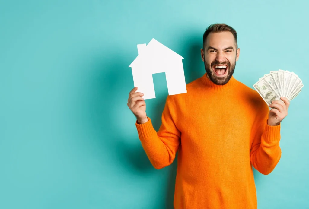 Homem comemorando segurando dinheiro na mão direita e o símbolo de uma casa com a esquerda. que com seu imovel quitado conseguiu um contratar o home Equity com juros mais baixos